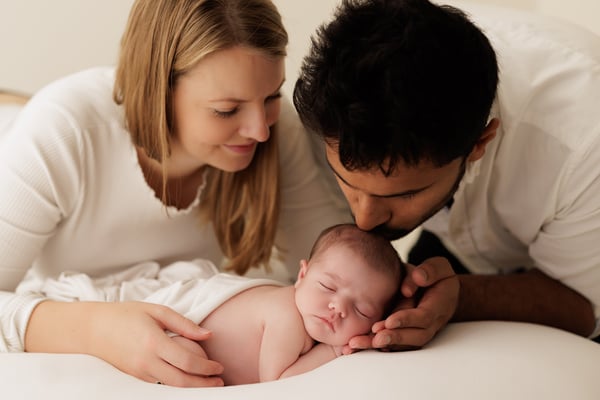 Both parents lying down and watching their newborn sleep between them