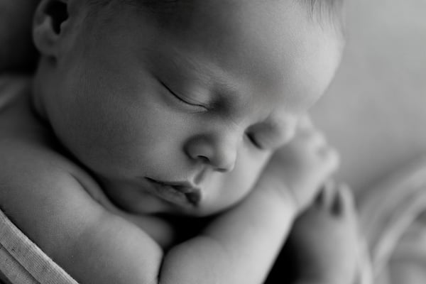 A sleeping newborn seen close, the face turned and both arms curled in
