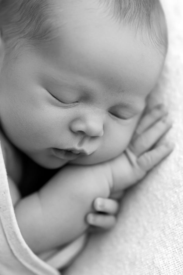 Close-up of a sleeping newborn's face, both hands drawn up under the chin