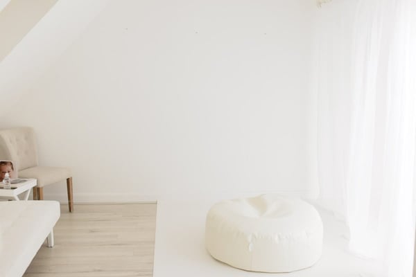 The shooting room: a cream beanbag on a white floor beside a sofa, lit by a sheer-curtained window