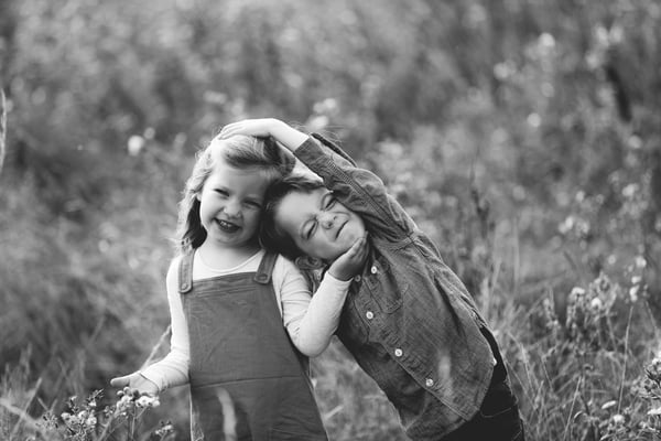 Two young children cheek to cheek and laughing in long grass, in black and white